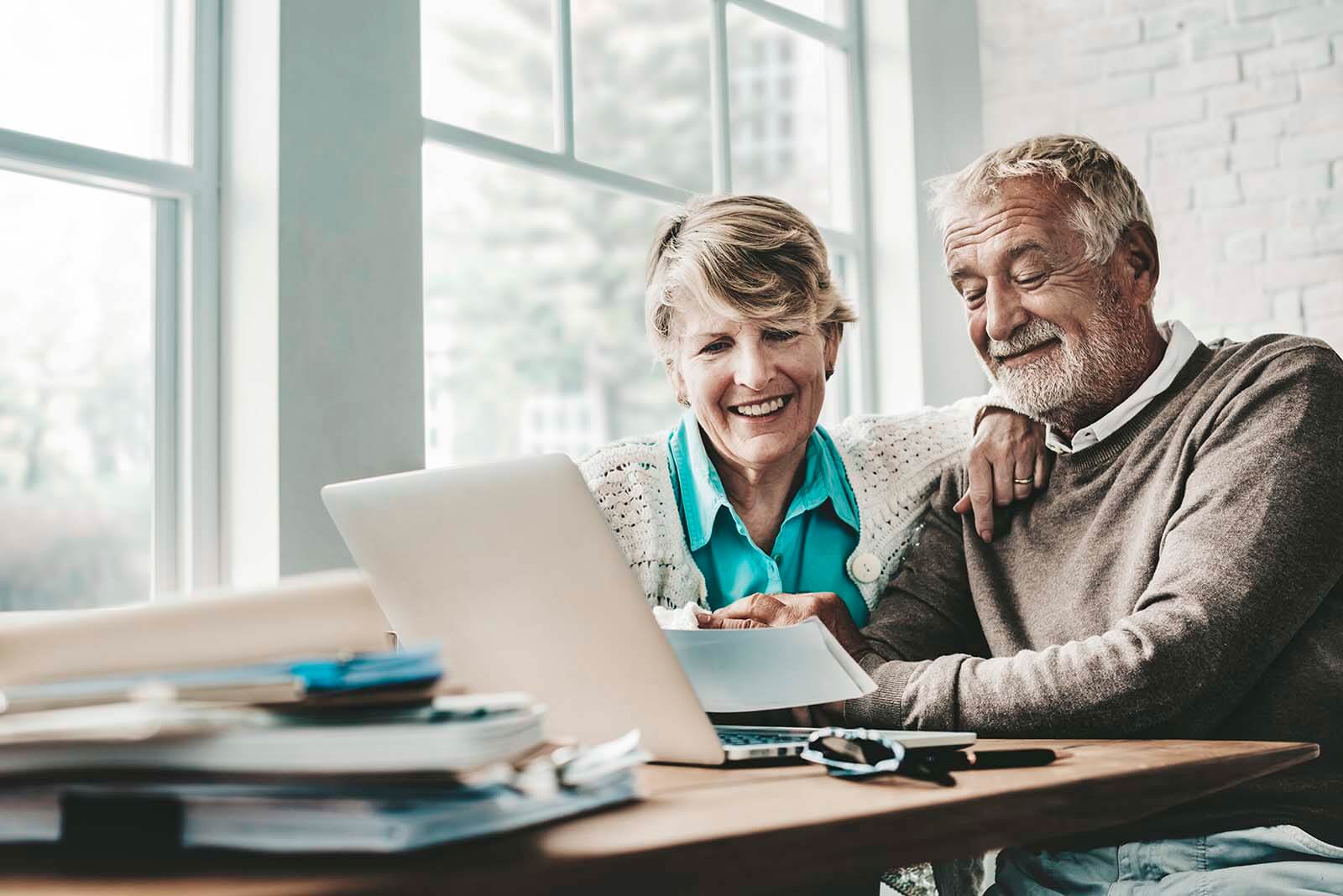 Relaxed mature couple sit with a laptop to review their portfolio with Via Wealth