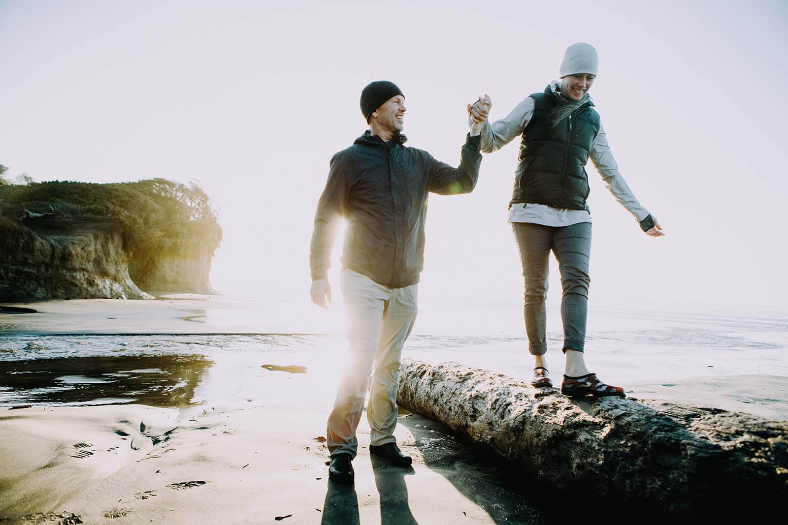 happy couple walk on the beach with sun in the background - Via Wealth